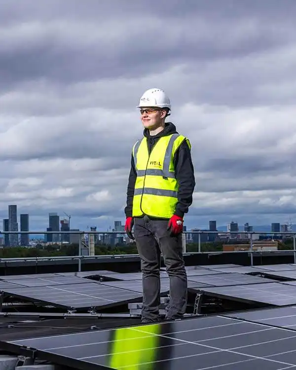 Electrical engineer inspecting solar panels on a rooftop while looking at the sky.
